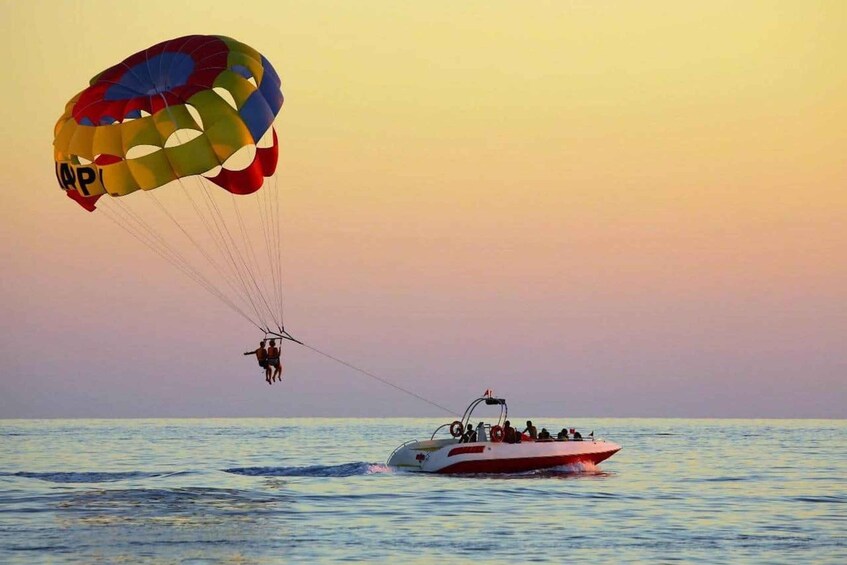 A parasail with a colorful canopy over the water, a person in a harness, and a speedboat with passengers. 1