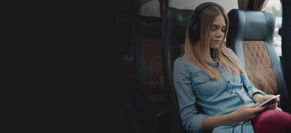 A person sitting in a vehicle, wearing headphones, and holding a device. 4