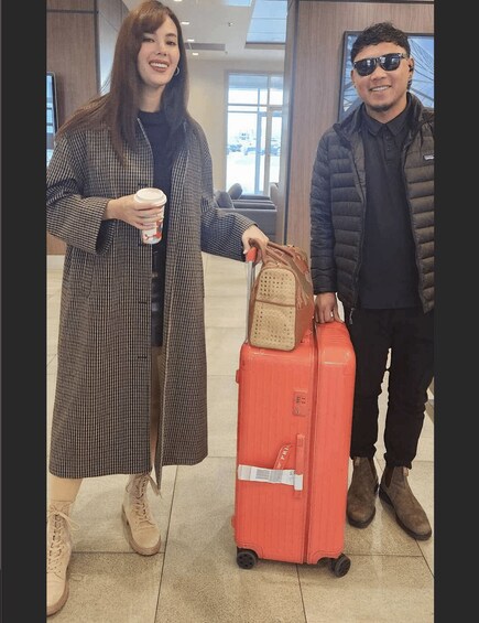 A person in a checkered coat holding a coffee cup and another person in a dark jacket with a suitcase. 2
