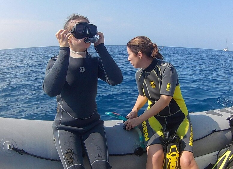 Two people in wetsuits sitting on a boat, preparing for a dive. 2