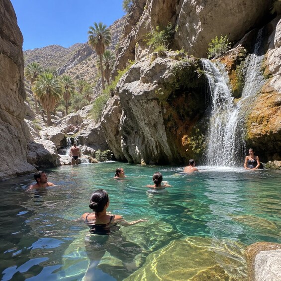 A natural hot spring with clear water, surrounded by rocky terrain and palm trees. 2