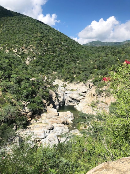 A rocky riverbed with a waterfall, surrounded by dense green vegetation and hills. 3