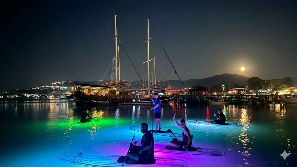 People sitting on a boat in a body of water at night with colorful lights. 2