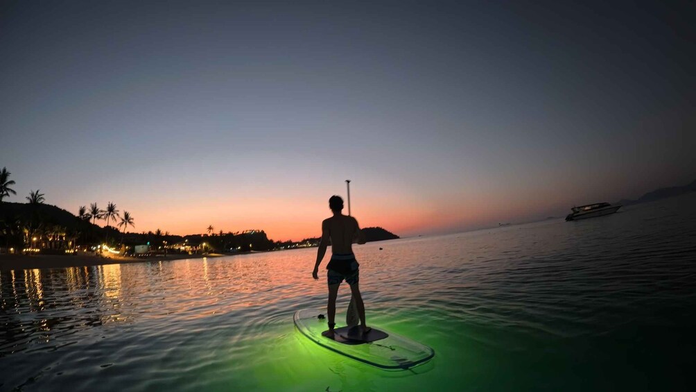 A person paddleboarding on calm water during sunset. 3
