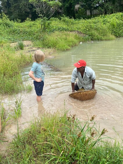 A person in a red cap and a child near a water body surrounded by greenery. 1