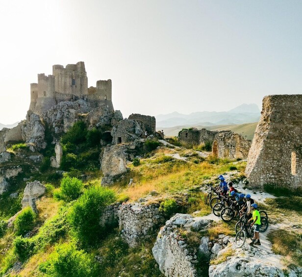 A group of cyclists on a trail with medieval ruins in the background. 2