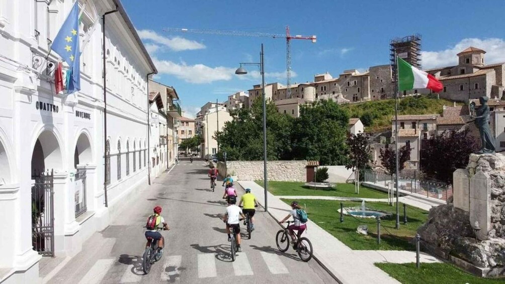 A street with cyclists, a fountain, and historic buildings. 4
