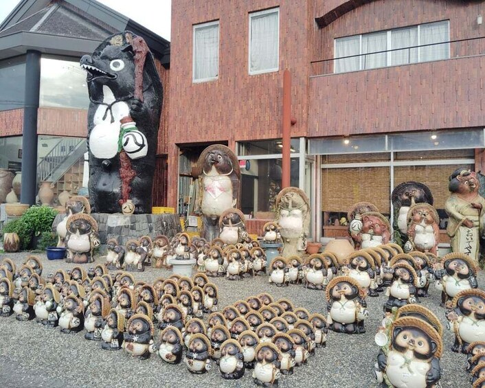A collection of ceramic figurines arranged in front of a building with a large black and white sculpture. 2