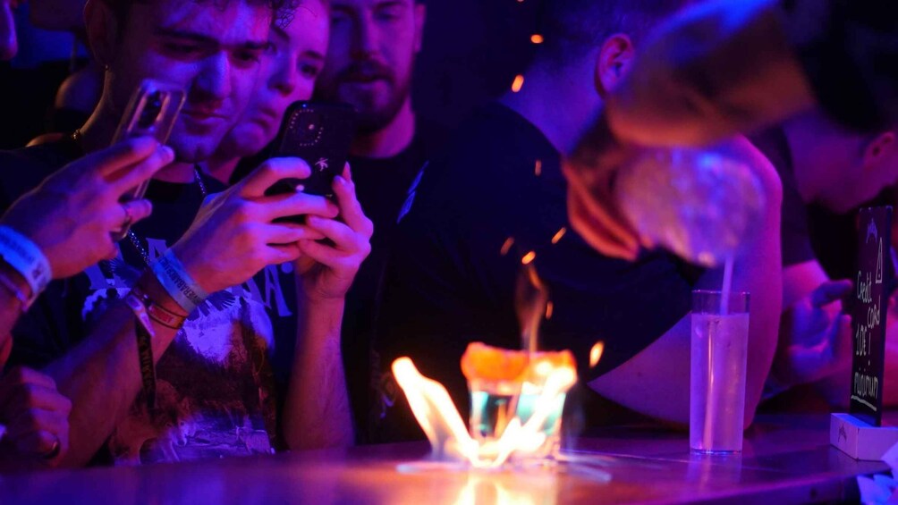 People at a bar with a fire in the center, a glass of water, and a bottle of alcohol. 2