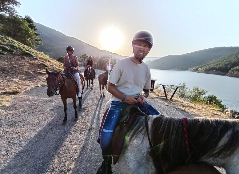 A person riding a horse on a dirt path by a lake with mountains in the background. 2