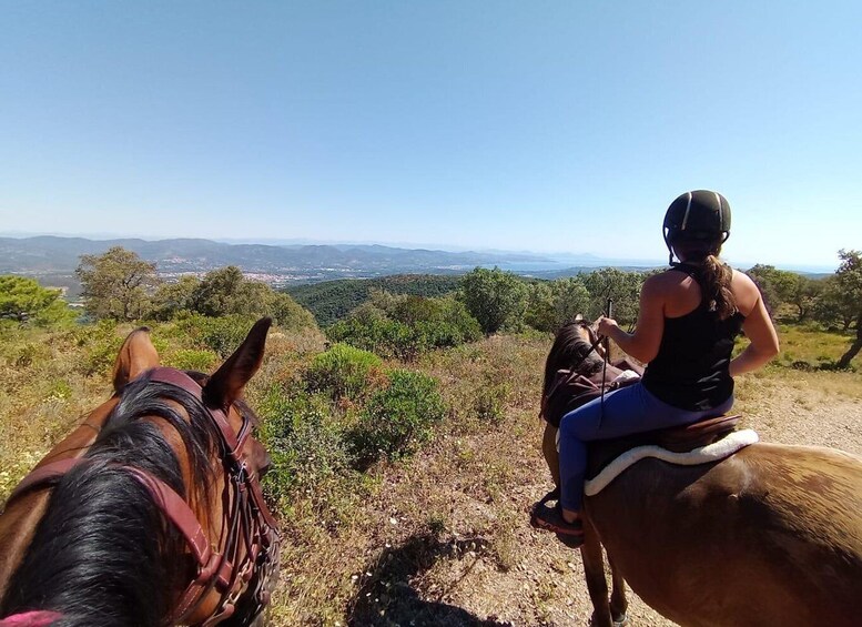 Two people riding horses on a hill with a view of a valley and distant mountains. 4