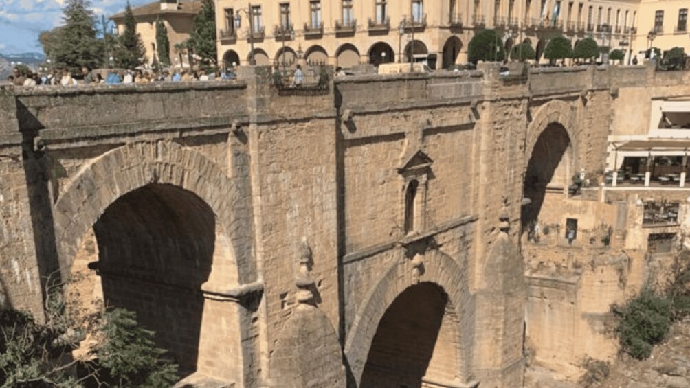 A stone aqueduct with multiple arches, a building with balconies in the background, and trees in the foreground. 4
