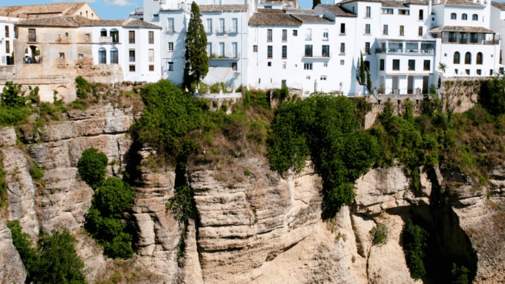 A coastal town with white buildings, rocky cliffs, and greenery. 1