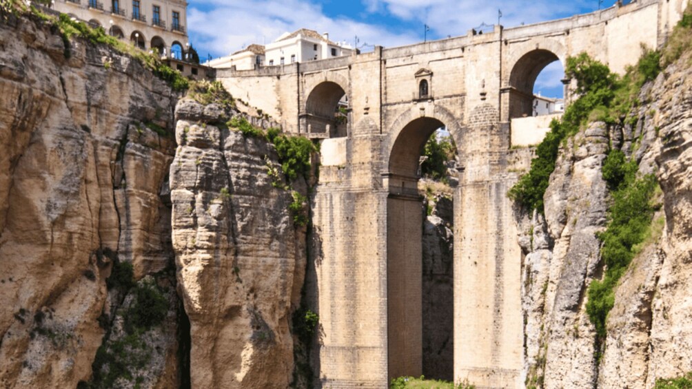 A stone bridge with arches spanning a rocky gorge, with buildings in the background. 2