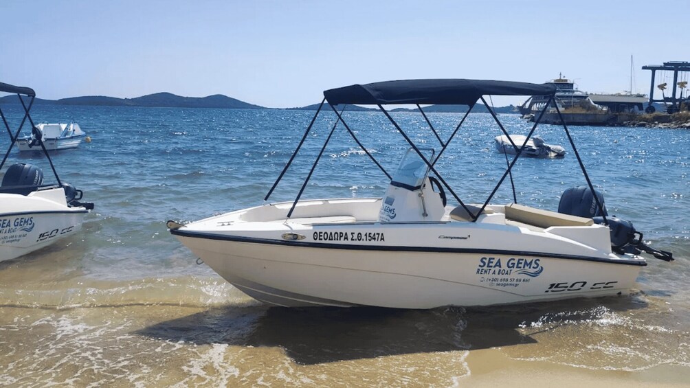A white boat named 'SEA GEMS' with a canopy, docked at a beach with other boats and a clear blue sky. 1