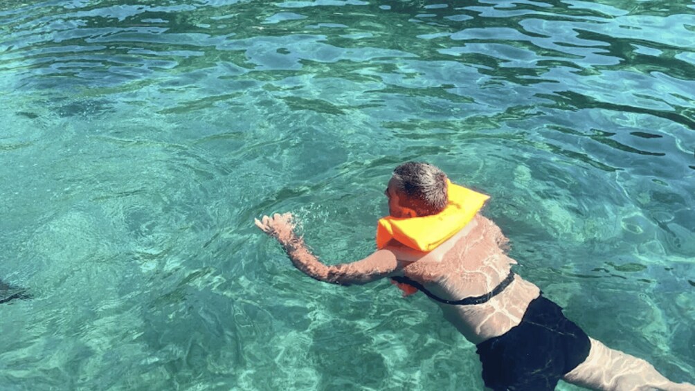 A person swimming in clear water with a yellow flotation device. 3