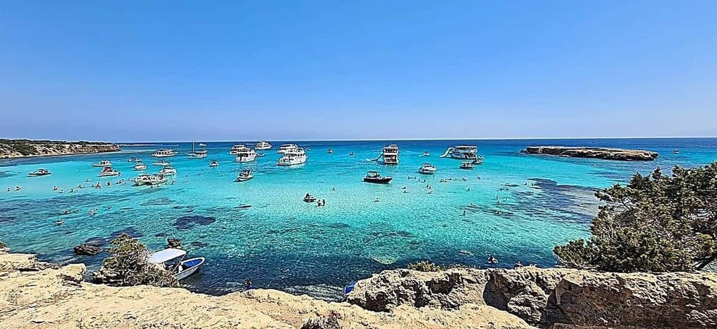 A coastal scene with boats, clear turquoise water, rocky shoreline, and sparse vegetation. 3