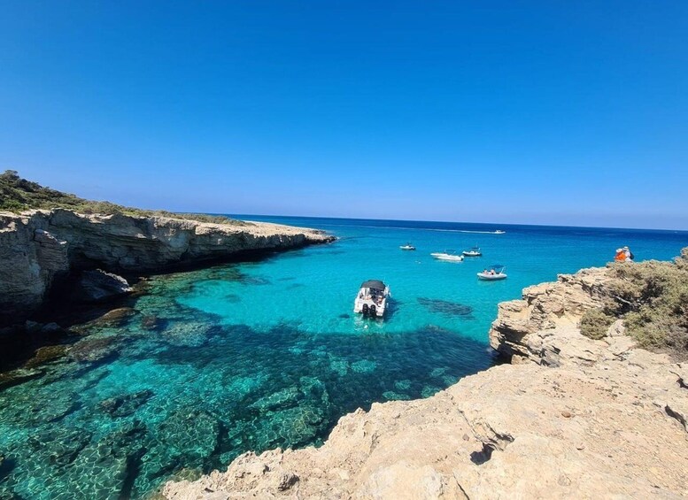 A coastal landscape with clear turquoise waters, rocky cliffs, and several boats anchored near the shore. 2