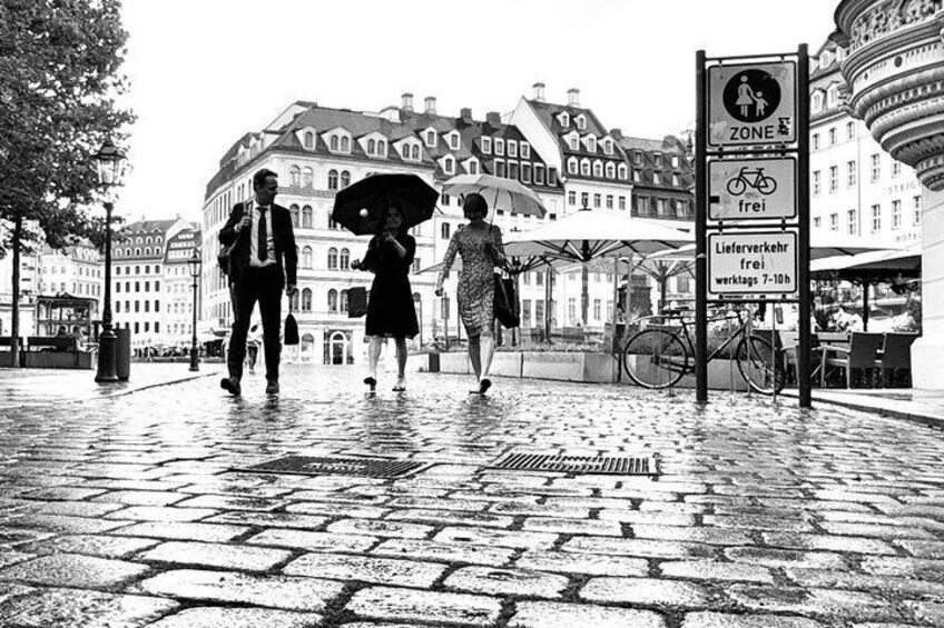 A cobblestone street with pedestrians, a bicycle, and a sign indicating a free delivery area. 2