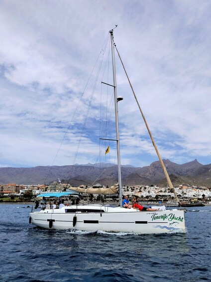 A sailboat named 'Tenerife Yacht' on calm waters with a mountainous backdrop and a coastal town. 2