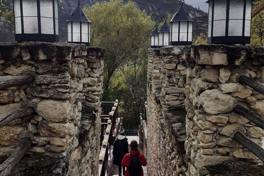 A stone pathway flanked by lanterns, leading through a narrow passage with a person in a red jacket and another in a black jacket. 4