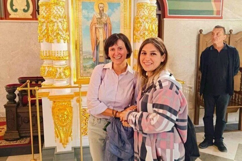 Two people standing in front of a religious icon with golden decorations. 1