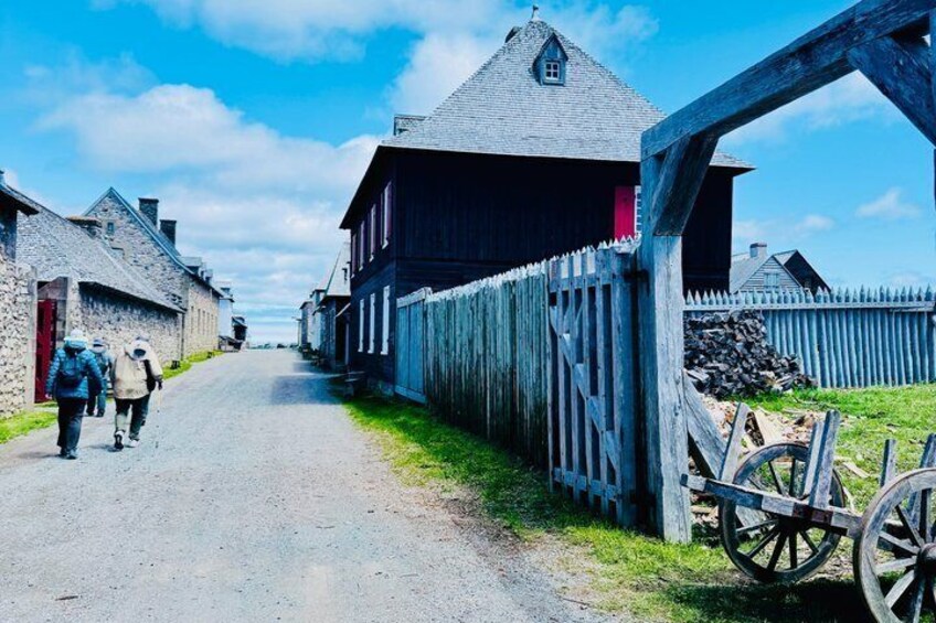 A rural street with wooden buildings, a wooden fence, and a cart. 5