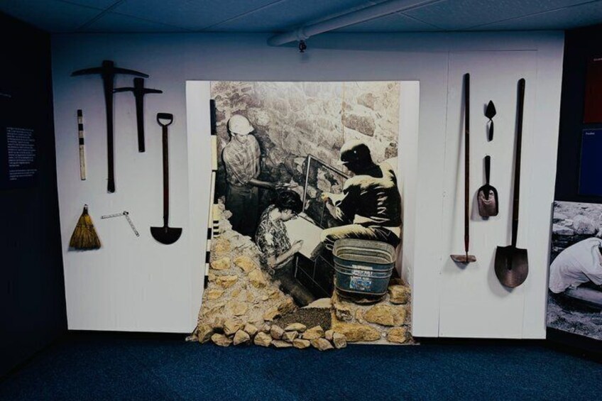 A room with a large painting of people working, surrounded by tools like shovels and a bucket. 2