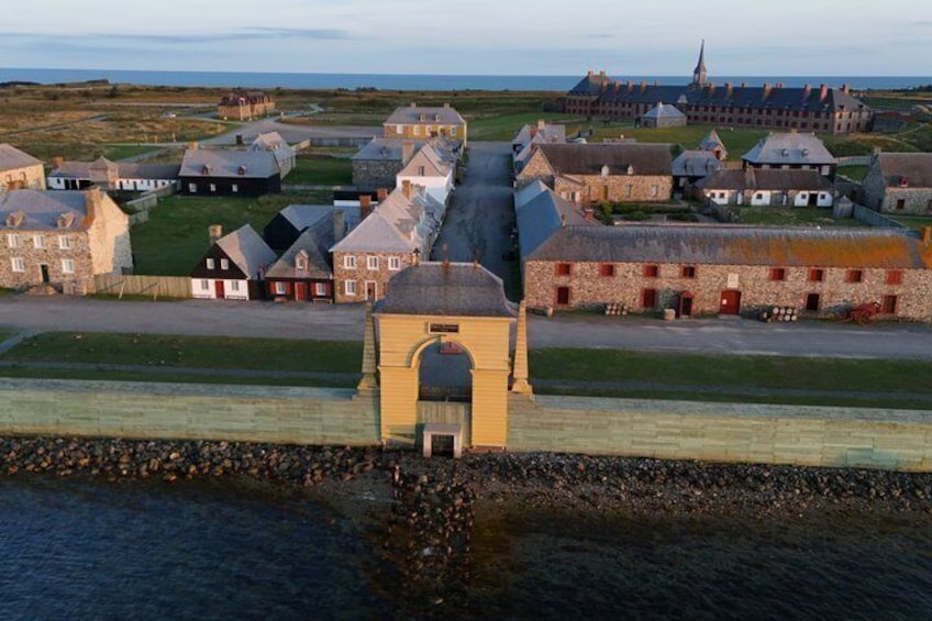 A coastal village with stone buildings, a prominent yellow tower, and a church in the background. 1