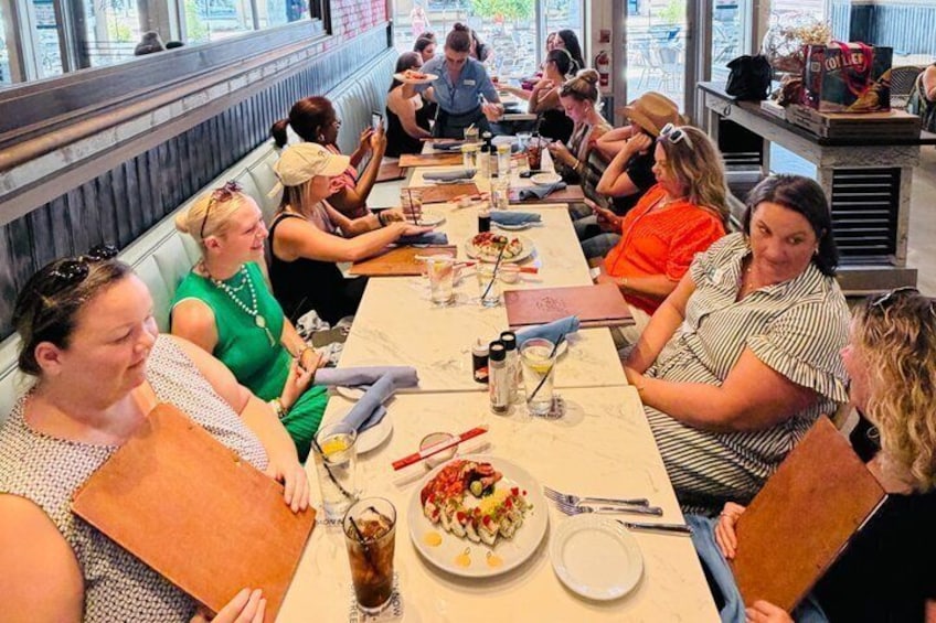 A group of people seated at a long table in a restaurant with various dishes and drinks. 5