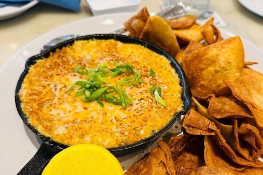 A skillet with a cheesy dish garnished with green onions, accompanied by tortilla chips. 2