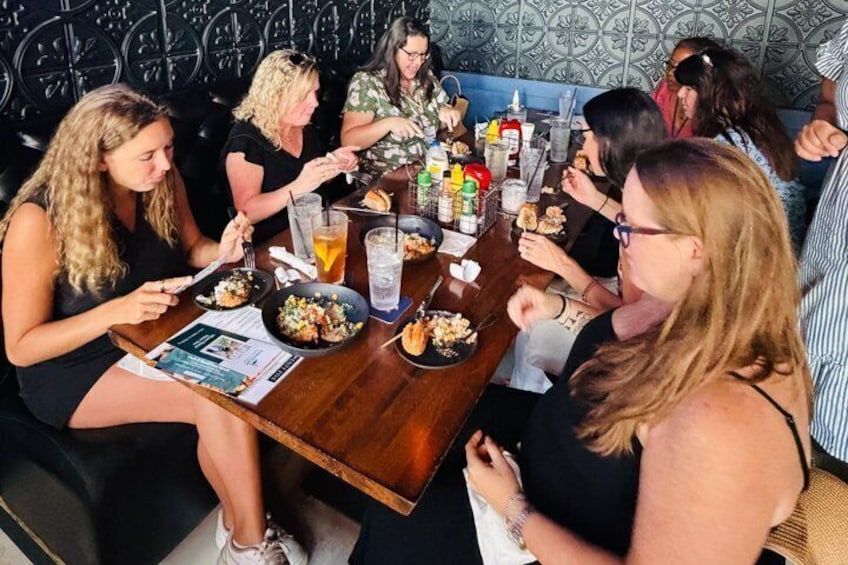 A group of people dining at a restaurant with a wooden table, plates of food, and condiments. 3