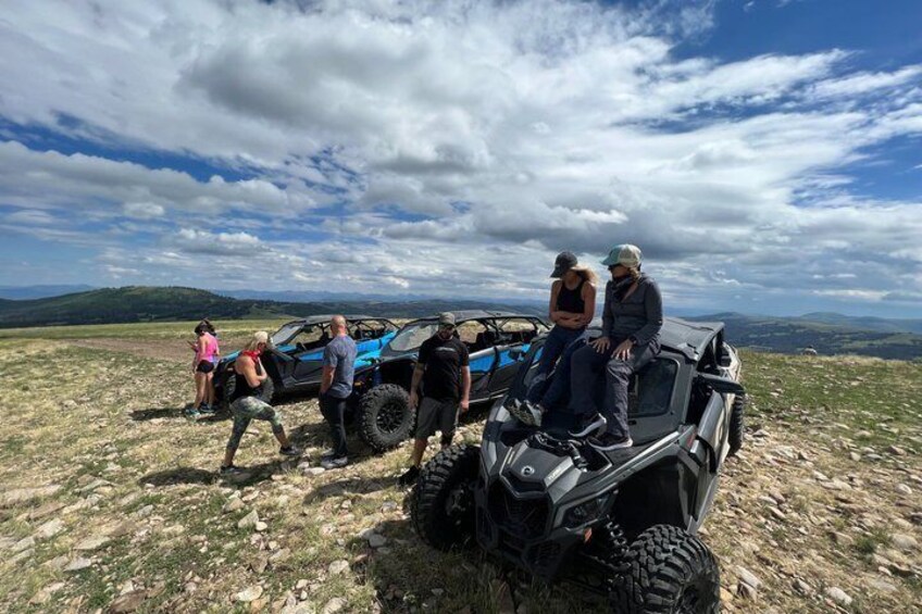 A group of people on a grassy field with ATVs, a clear sky, and distant hills. 2