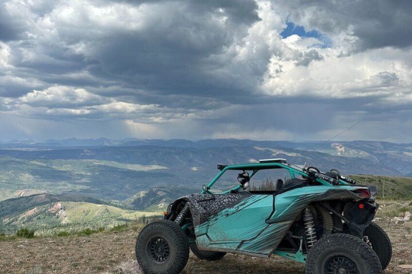 A teal off-road vehicle parked on a hill with a mountainous landscape in the background. 4