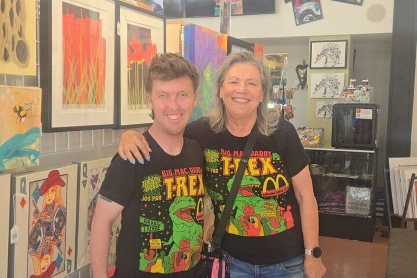 Two people standing in a room with colorful artwork on the walls. 4