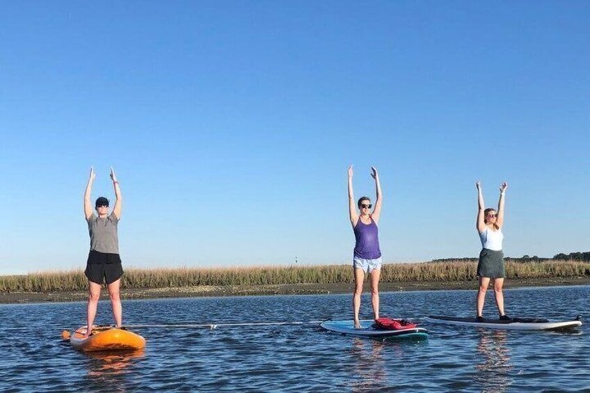 Three people paddleboarding on a calm body of water with a clear sky and a distant shoreline. 1