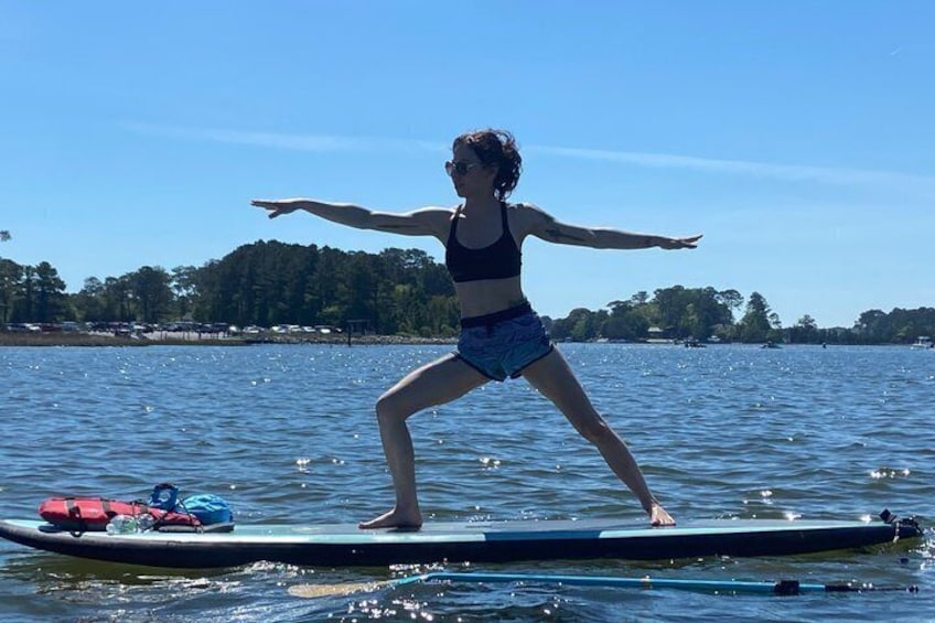 A person standing on a paddleboard in a body of water with trees and buildings in the background. 2