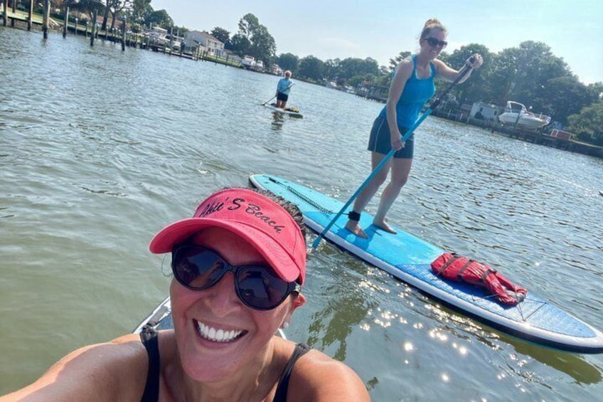 A person paddleboarding on a calm body of water with another person in the background. 2
