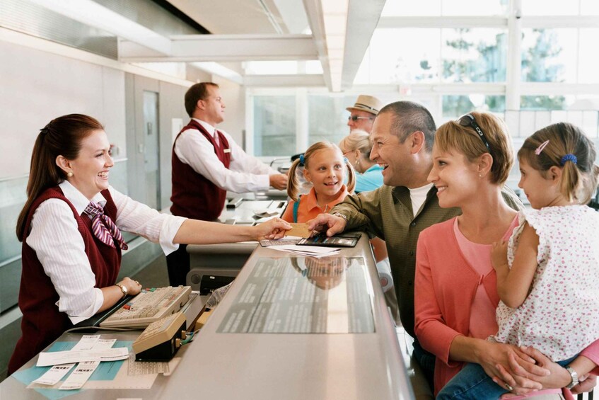 A ticket counter with a ticket machine, a person handing out tickets, and several people waiting in line. 3