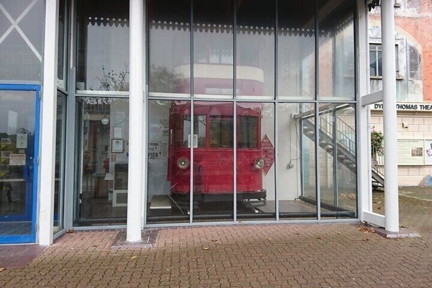 A red tram inside a glass-walled building with a blue door and a staircase to the right. 2