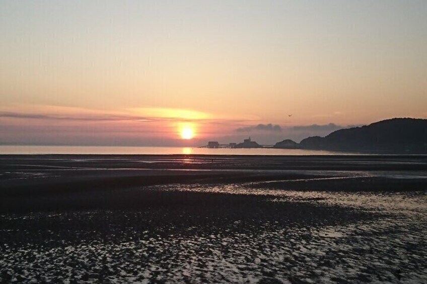 A sunset over a beach with calm waters and distant hills. 3
