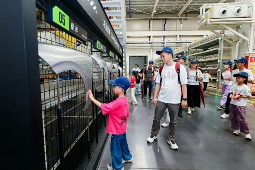 A group of people in an industrial setting, some wearing safety helmets and caps, interacting with machinery. 5