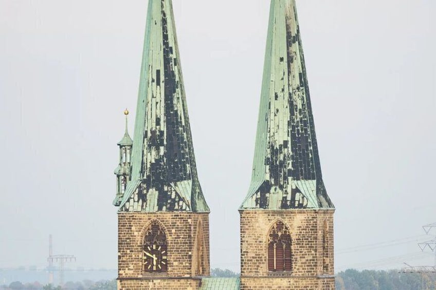 Two tall, pointed towers with green roofs, one with a clock and a smaller tower with a weather vane. 2