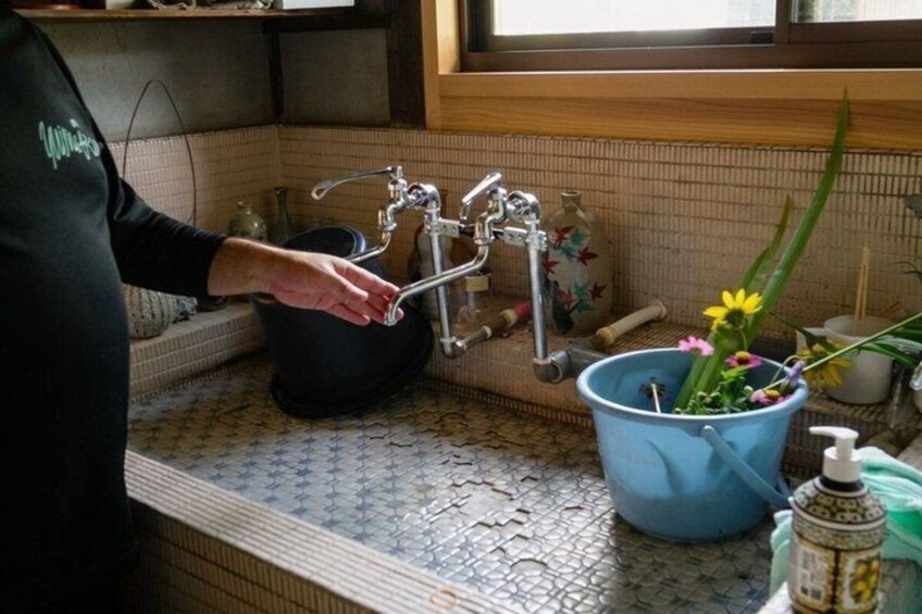 A person adjusting a faucet in a kitchen with a blue bucket containing flowers and a bottle of dish soap on the counter. 5