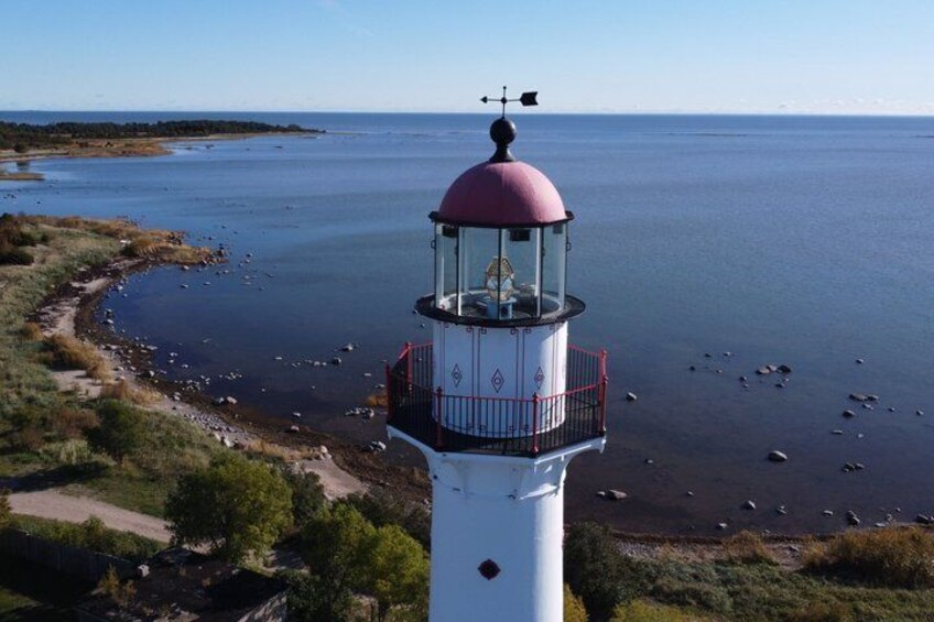 A lighthouse with a red top, surrounded by a rocky shoreline and calm water. 4