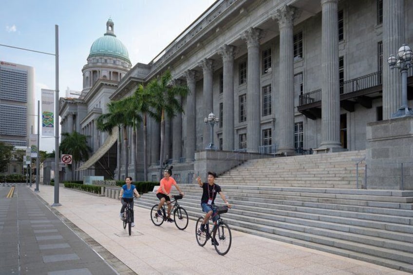 Three cyclists on a sidewalk in front of a large building with columns and a dome. 5