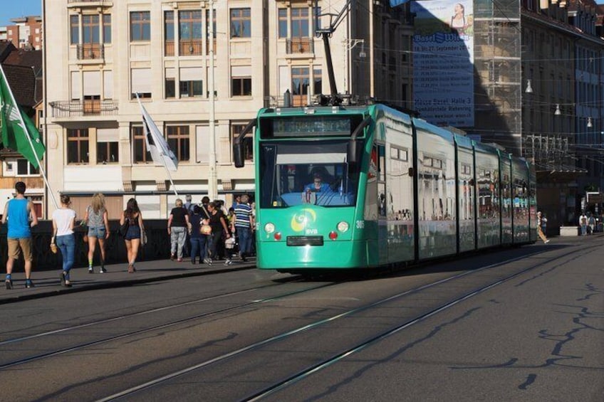 A green tram on tracks with people walking on the sidewalk. 3