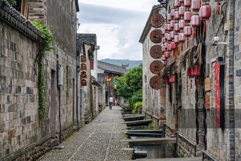 A narrow cobblestone street flanked by traditional stone buildings with red lanterns and signage. 5