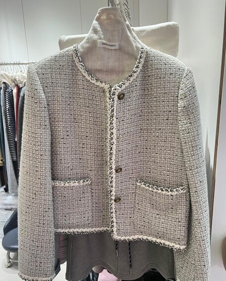 A gray knitted jacket with a white trim and buttons, hanging on a mannequin in a store. 5