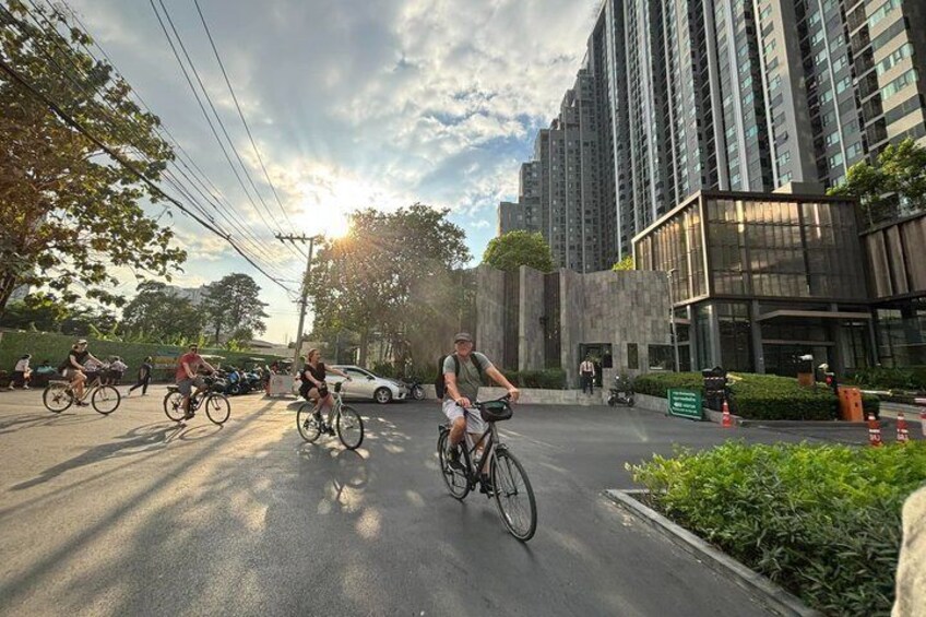 Cyclists on a road with buildings and greenery in the background. 3
